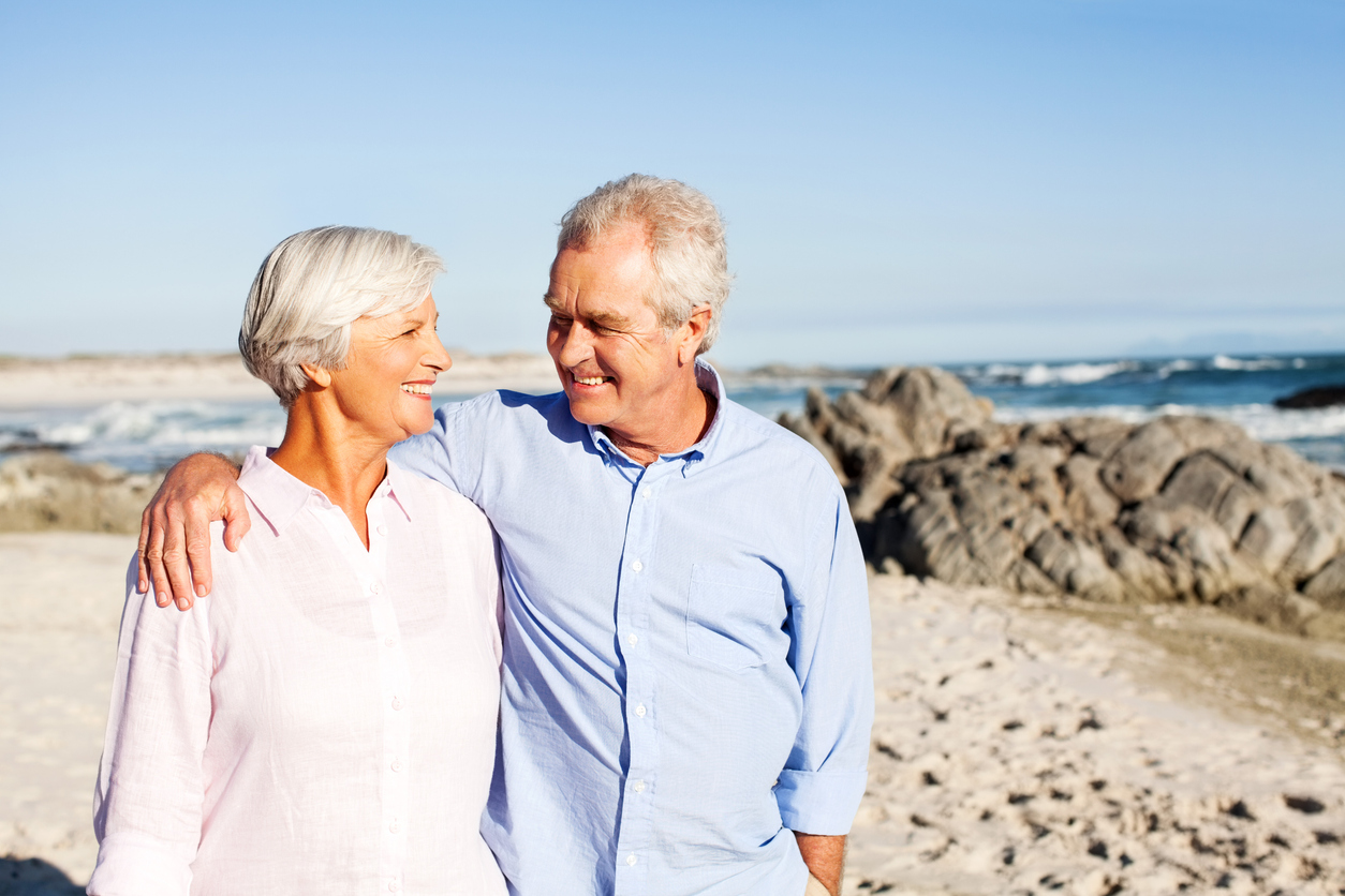 senior man with arm around woman walking on beach